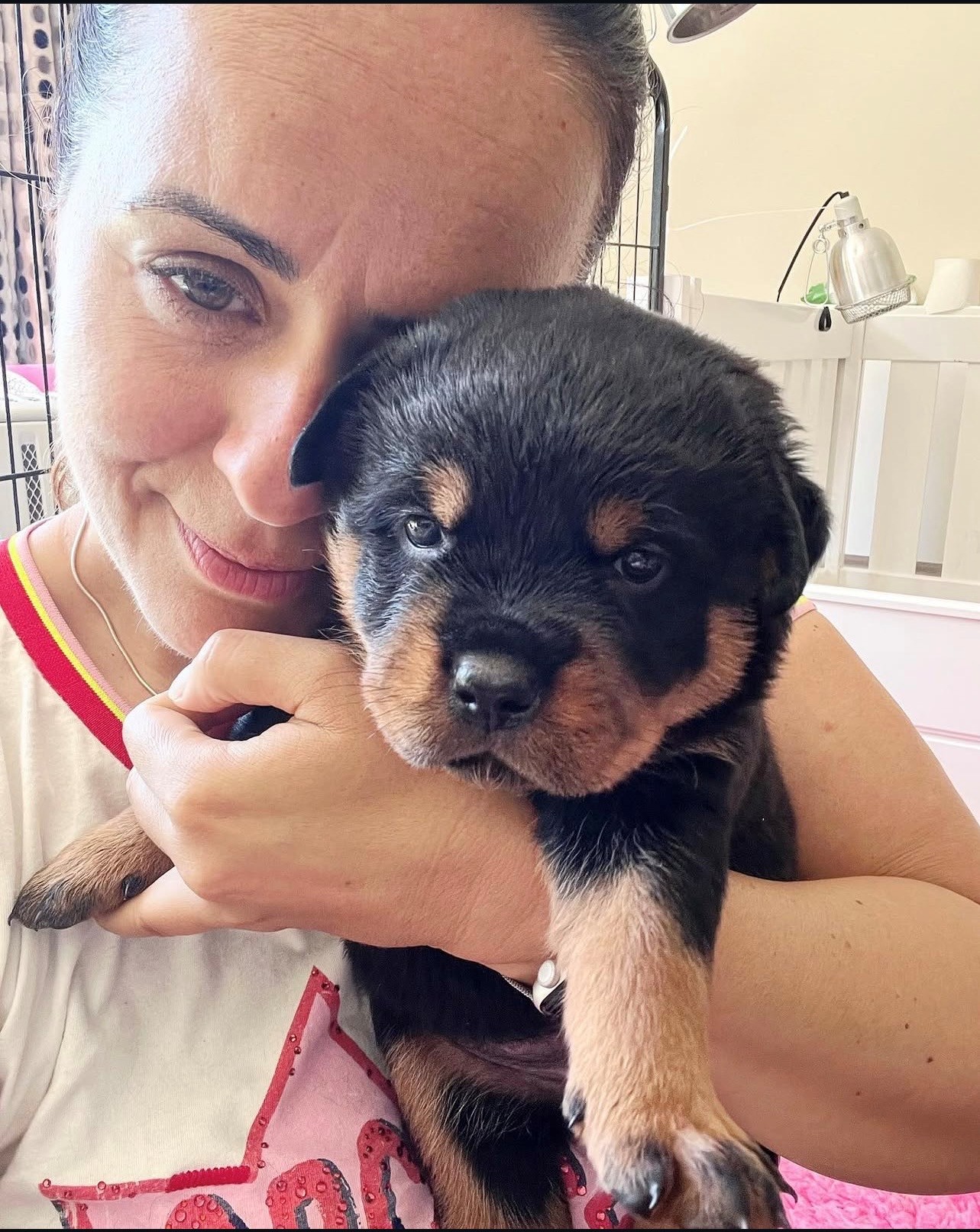 Woman cuddles a small black-and-tan puppy indoors, holding it close with a gentle smile.
